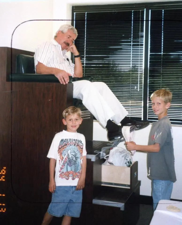 A young boy shining an older man's shoes — a quiet moment of service and care passed between generations